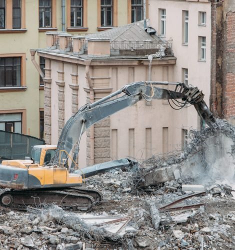 Building of the former hotel demolition for new construction, using a special hydraulic excavator-destroyer. Complete highly mechanized demolition of building structures. Construction site concept