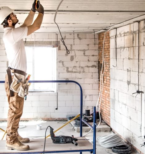 Electrician installer with a tool in his hands, working with cable on the construction site. Repair and handyman concept. House and house reconstruction.